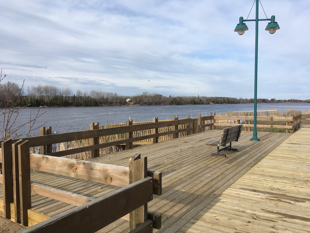 a wooden boardwalk overlooking a lake with a bench