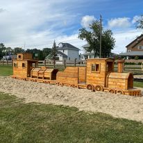 a wooden train on a bed of sand surrounded by grass