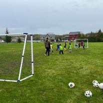 kids playing soccer outside on a green field with 2 goal posts