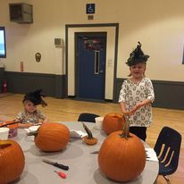 two little girls with green triangle hats and a table with pumpkins on it
