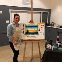 woman showing a painting of a sunset on an easel