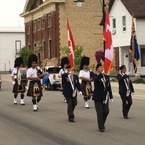 marching band with 3 men bearing flags in front and 2 men with bagpipes in the next row and 2 men with drums in the third row