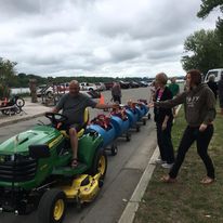 man driving a tractor pulling a train of smaller cars with kids riding in the cars with two women on the side