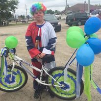 kid dressed like a clown posing with a bike with balloons attached to it