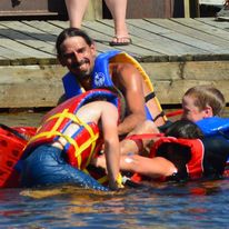 1 man and 2 kids playing on the water wearing lifevests