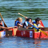 2 boys in a boat rowing forward and 2 girls on a boat going perpendicular
