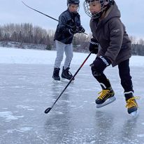 2 kids playing hockey on the ice outside