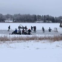 wideshot of people playing hockey outside with a small group of people watching