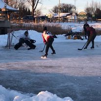 3 people playing hockey outside where 2 are players and 1 is a goalie